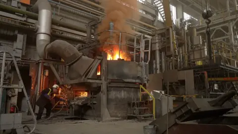 As material is added to the molten steel, a flame is generated at the top of the arc furnace.
