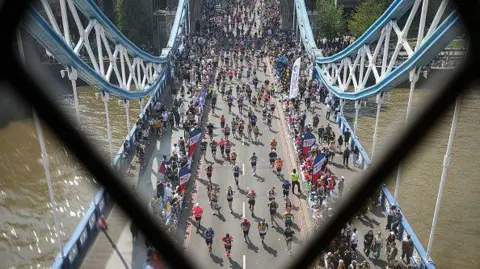 Getty Thousands of runners cross Tower Bridge during the London Marathon, viewed from above, with spectators lining both sides of the roadway.