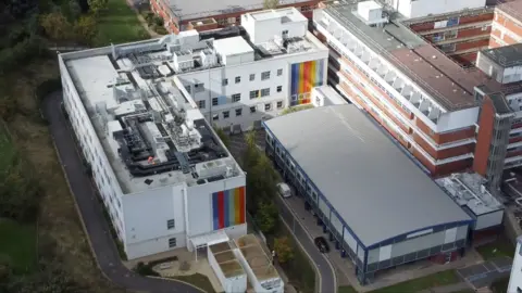 Dawid Wojtowicz/BBC The children's ward at Kettering General Hospital from the air. The image shows a white building on the side of the main hospital with rainbow stripes on the cladding. The hospital has a flat roof.