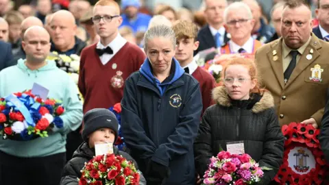 Pacemaker Two children hold bouquets of flowers with a large crowd of people behind them