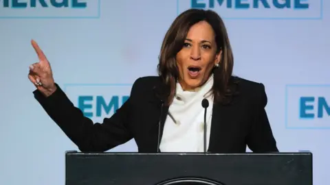 Kamala Harris speaking on stage at podium with finger pointed in the air