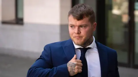 A man wearing a blue suit jacket, white shirt and black tie. He is looking over his right shoulder