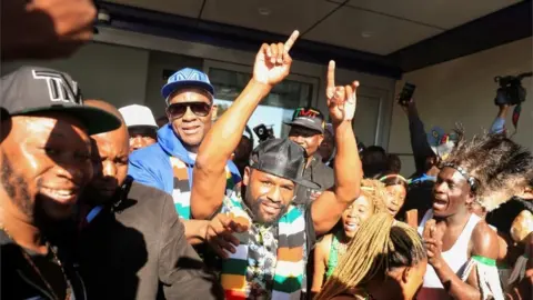 Philimon Bulawayo/Reuters Floyd Mayweather gestures to fans upon his arrival at Robert Gabriel Mugabe International Airport in Harare, Zimbabwe, on 13 July.