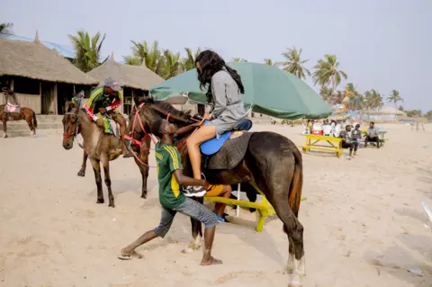 Grace Ekpu/BBC Woman being helped onto a horse