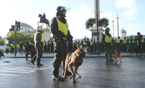 Lucy North / PA Media A police officer with a riot helmet stands on a street next to Trafalgar Square with the statues and museum in the background, with crowds of officers in reflective uniform in the background, during a Unite the Kingdom protest in September.