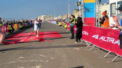 Alison Ferns/BBC Christa Cain crossing the finishing line of the Brighton Half Marathon.