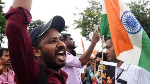 A protester, wearing a red shirt and a black cap, shouts slogans during a demonstration in Ranchi