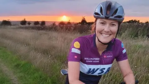 Angela Mills-Bannon in a purple cycle top staring at the camera while sat on her bike in a field