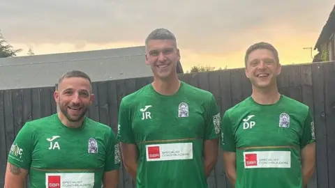 Three football coaches (left to right) Jake Anderson, James Robinson and Dave Pearson wearing green Chipping FC football tops standing in a garden with a wooden fence behind them as the sun sets. They are all smiling.