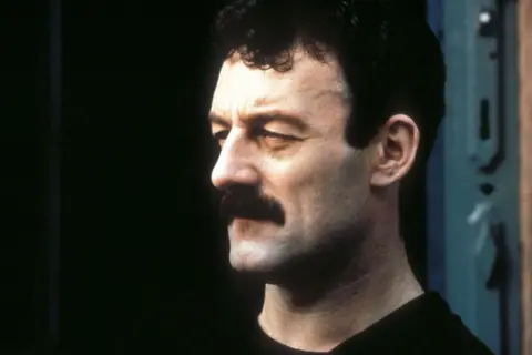 A still of Bernard Hill in characters as Yosser Hughes - he is facing side-on, sporting a thick black moustache.