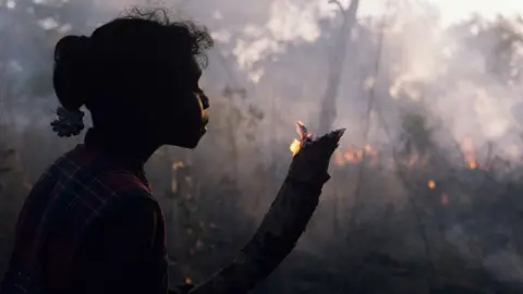 Getty Images A girl in Arnhem Land, Australia, holds a small branch which flickers with flame