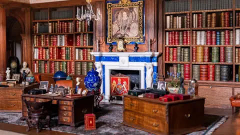 His Majesty King Charles III 2024/PA miniature library with shelves stacked with tiny books and a fireplace