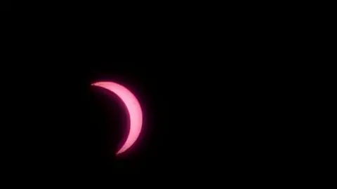 A view of the sun, which appears pink in colour, and is partially covered by the moon.