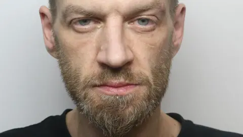 A man with a beard and wearing a black t-shirt.