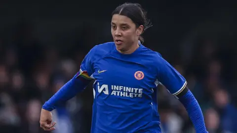 PA Media Sam Kerr on the pitch playing football. She wears a blue Chelses football strip and her dark hair is tied back as she runs forwards