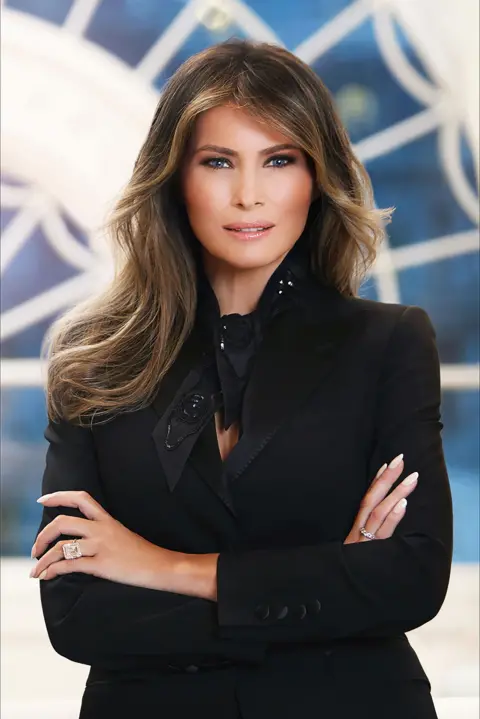 White House / Régine Mahaux Mrs Trump folds her arms in front of a white and blue background