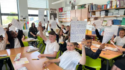 BBC Children hold up the letters they've written, whilst sitting in their classroom