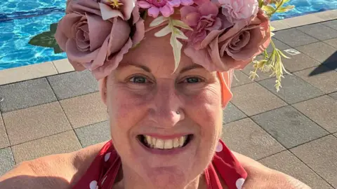 Megan Studholme-Dooley A selfie-style picture of Megan Studholme-Dooley, who is wearing a red polka-dot swimming costume and a floral hat. She is standing on the edge of the pool.