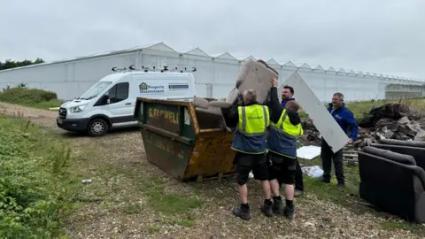 Double H Nurseries Three men are lifting a sofa into a skip. A white van is pictured in the background.