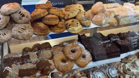 Steele's Family Bakery Baked goods behind a glass cabinet, including chocolate jam doughnuts, scones, Eccles cakes and chocolate brownies.