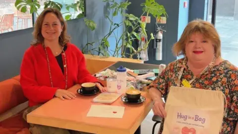 Two women sitting either side of a table in a coffee shop. One i s