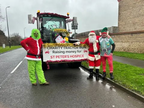 George Atwell Three men dressed as the Grinch, Father Christmas and an elf are standing near a tractor which says Charity Tractor Run Raising money for St Peter's Hospice