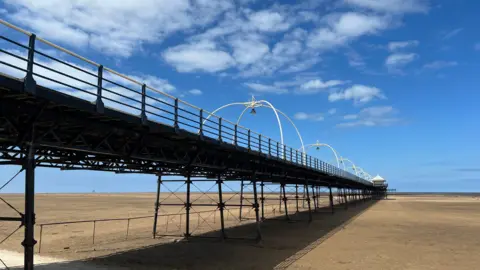 BBC/Claire Hamilton Southport pier taken from below on the beach - golden sand stretches out to the sea which is far away