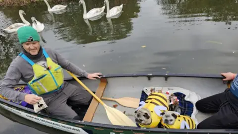 Lara King Two dogs in a canoe with a man on the river