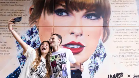 PA Two people take a selfie in front of a Taylor Swift mural