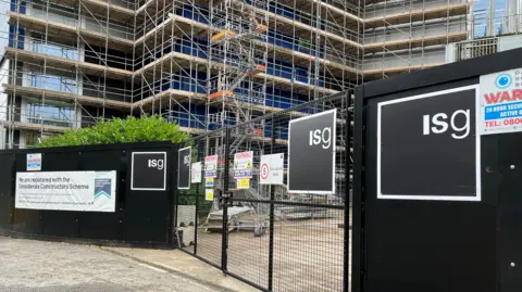 Black hoardings with ISG branding surround the former Ikea building. The building is visible behind and is covered in scaffolding.