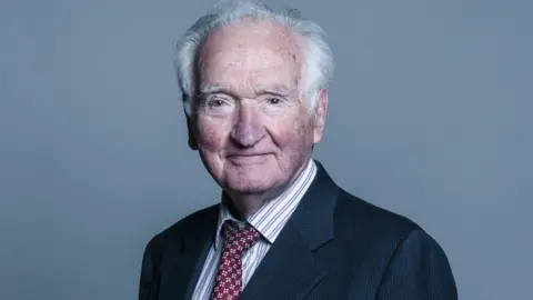 Lord Mackay has thinning grey hair and is wearing a business suit, in a portrait photograph 
