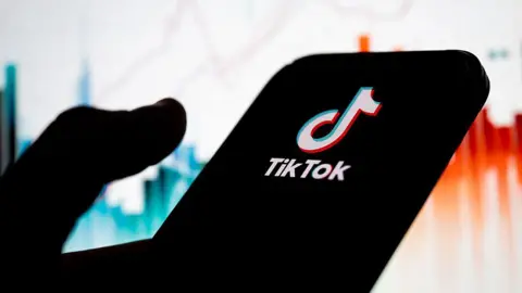 The TikTok logo on a phone in a person's hand.