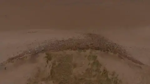 National Trust An aerial picture of a stretch of beach with rubble curving around a sand dune 