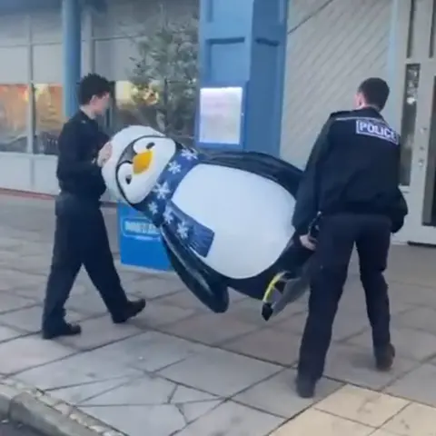 Prezzo Two police officers carrying a large penguin decoration towards a restaurant.