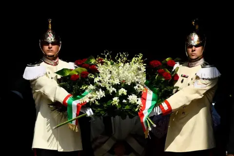 Stefano Guidi / Getty Images Flowers are carried ahead of Silvio Berlusconi's coffin as it is brought out of Milan's cathedral - the Duomo di Milano - for his state funeral