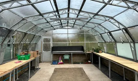 The interior of a large empty greenhouse with wooden tables down either side