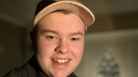Harry Boulton Picture of Harry. Faired haired, close up, smiling wearing a cap. lighting is dim with a soft focus on Harry's face.