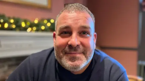 Scott Blackwell who has short grey hair and a beard and moustache,  smiling at the camera