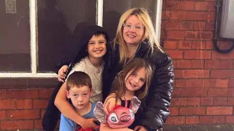 Mum cuddling her three kids near wall