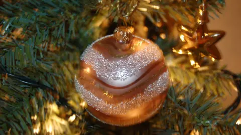 BBC A picture of a bauble hanging on a Christmas tree. It is a shiny silver and bronze colour.