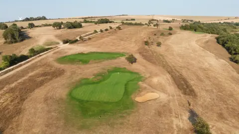 An arial view of a golf course. Only the greens appear healthy and green, with the rest of the course looking dry and brown.