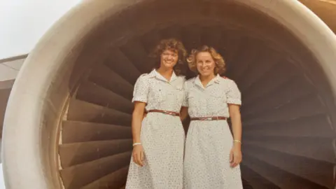 Claire O'Donnell An archive image of Claire O'Donnell from her flight attendant days posing with another flight attendant in front of a plane engine. They are both wearing white dresses with dots.