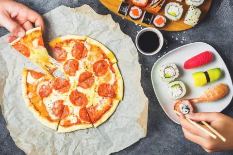 Getty Images A man eating pizza while a woman has sushi