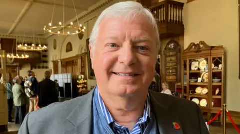 A man stood inside a historic building, wearing a grey suit. Councillor Alan Amos is inside the Guildhall in Worcester.