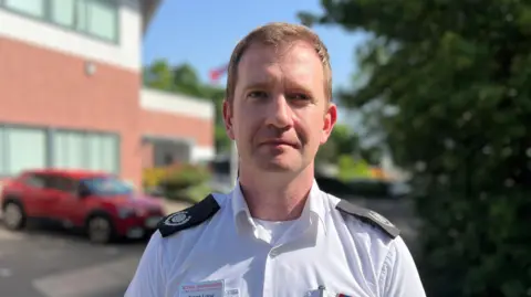 Frank Long is wearing a formal fire service uniform. It's a white shirt buttoned down the middle with black epaulettes. 