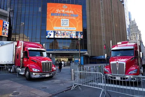Reuters Two red semi-trucks are parked outside an entrance to the venue that has the words 'Pennsylvania Station' above the entrance, with a billboard above advertising a basketball camp.