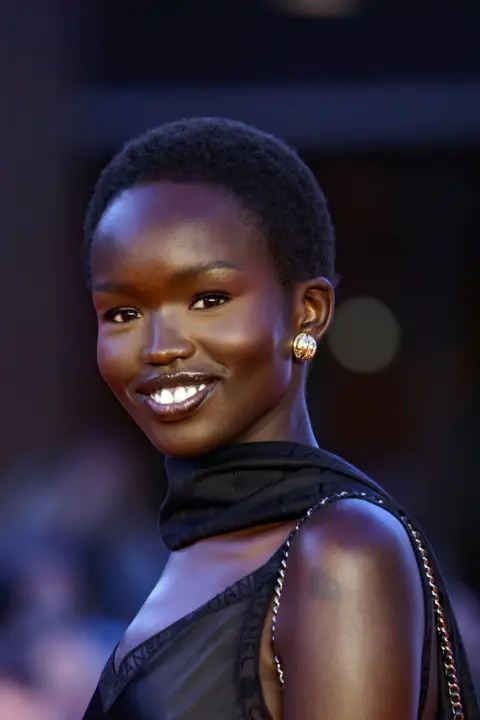 FABIO FRUSTACI / EPA A woman wearing a black dress stands on the red carpet and poses for cameras.
