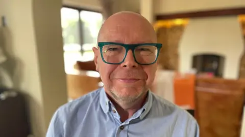 A man with glasses, wearing a blue shirt, looking at the camera