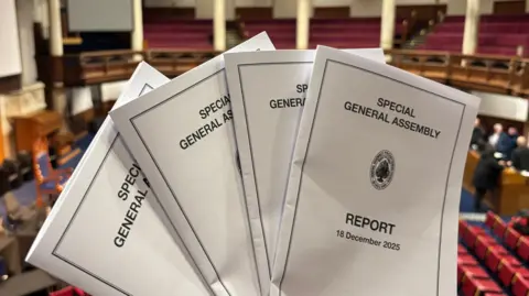 Photo of a bunch of paper reports that read Special General Assembly Report 18 December 2025. 
