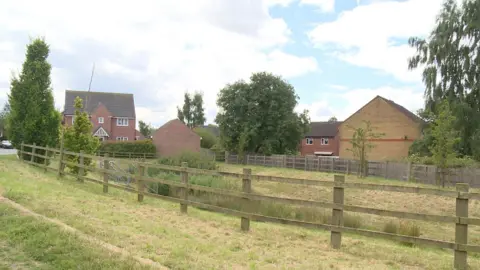 BBC A picture of a balancing pond and fence on a new-build housing estate 